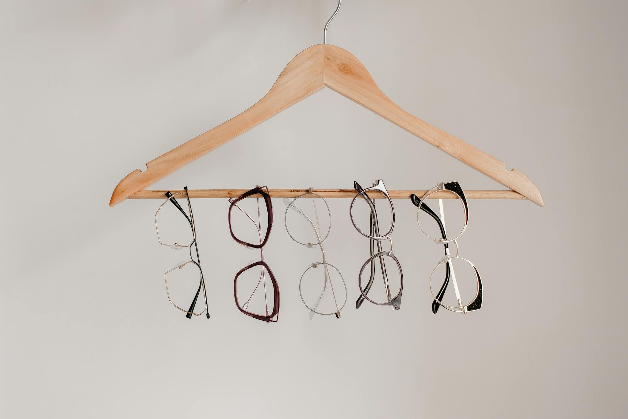 Various eyeglasses frames neatly hanging on a wooden clothes hanger with neutral background.